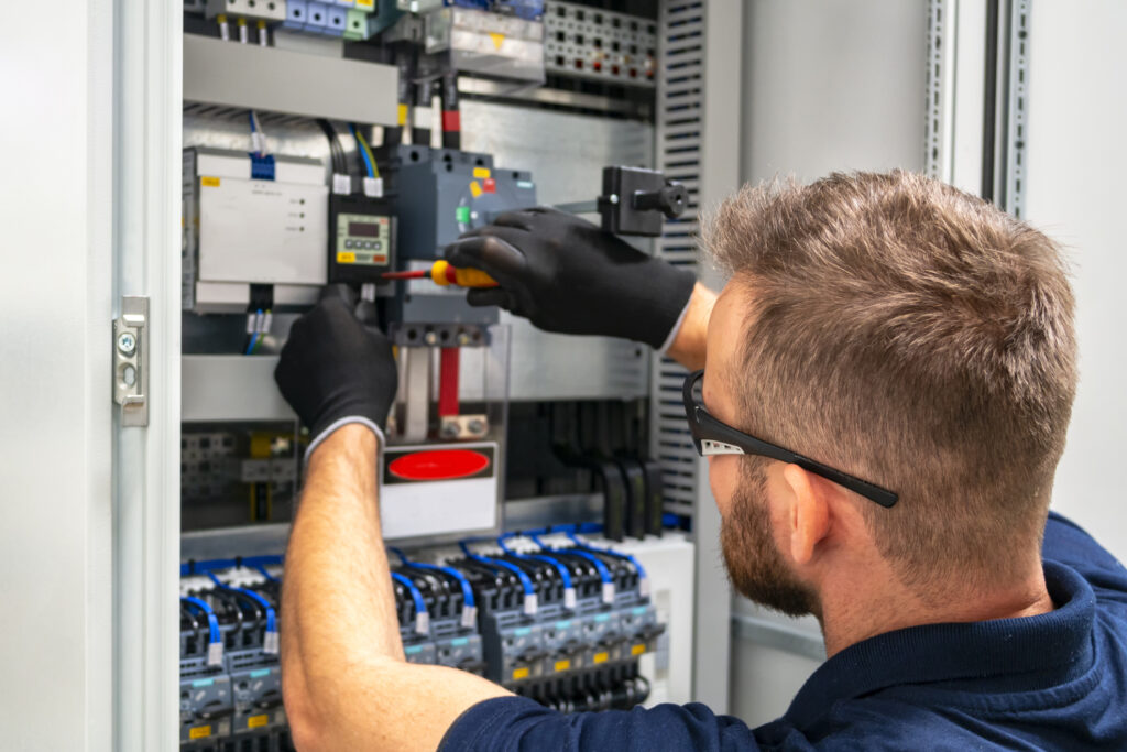 Tecnico al lavoro su un quadro elettrico con guanti isolanti e cacciavite