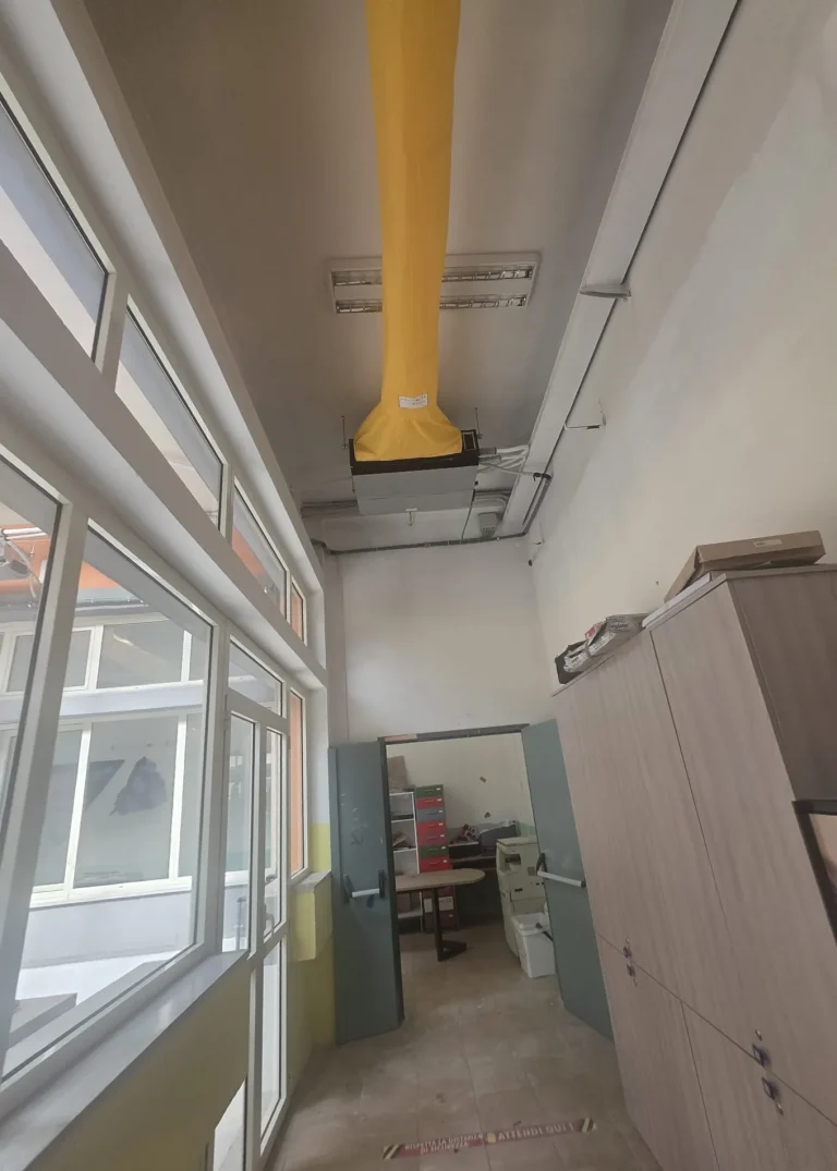 Diffusore tessile giallo collegato all’unità canalizzabile a soffitto in un ambiente scolastico