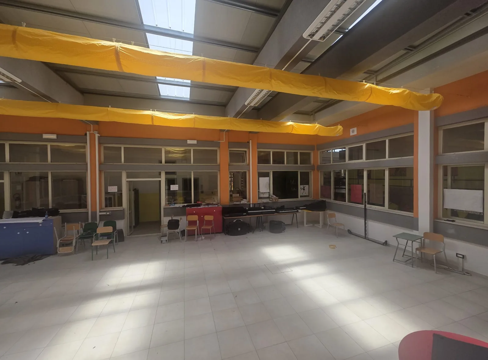 Salone polifunzionale della scuola Brugnano con due file di canali tessili a soffitto, illuminato dai lucernari